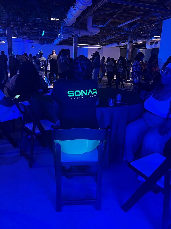 A large hall lit deep blue with the Sonar booth and a crowd behind