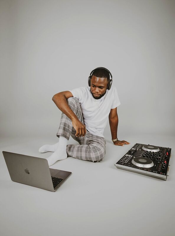 A DJ seated on the floor with a laptop and controller
