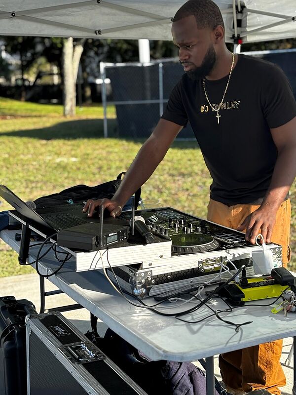 A DJ working turntables under a white tent in daylight
