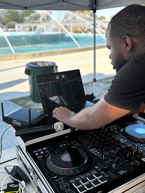 A DJ working a controller outdoors with a fountain behind