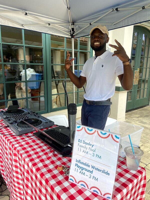 A DJ at an outdoor family day beside a schedule sign