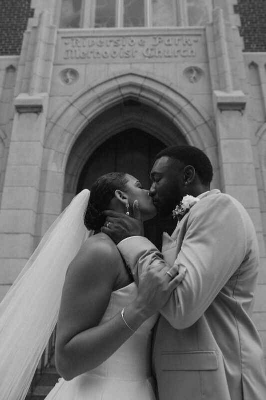 Black and white photograph of a couple kissing in a stone church doorway
