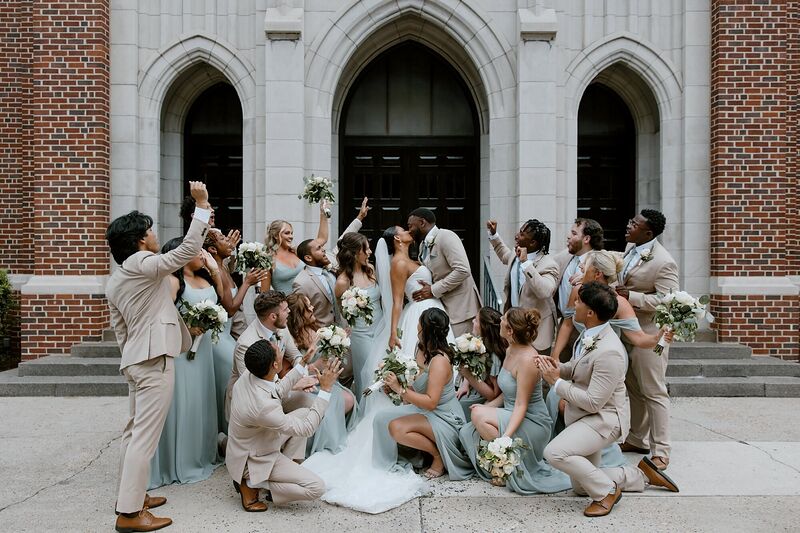 A wedding party cheering around the newlyweds on church steps
