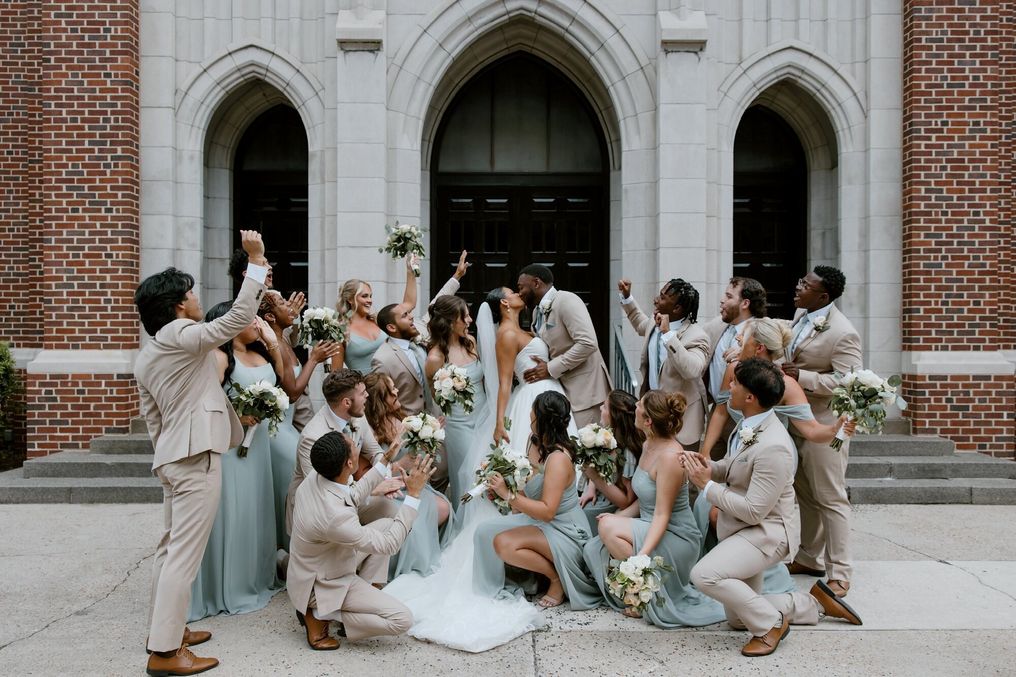 A wedding party cheering around the newlyweds on the church steps