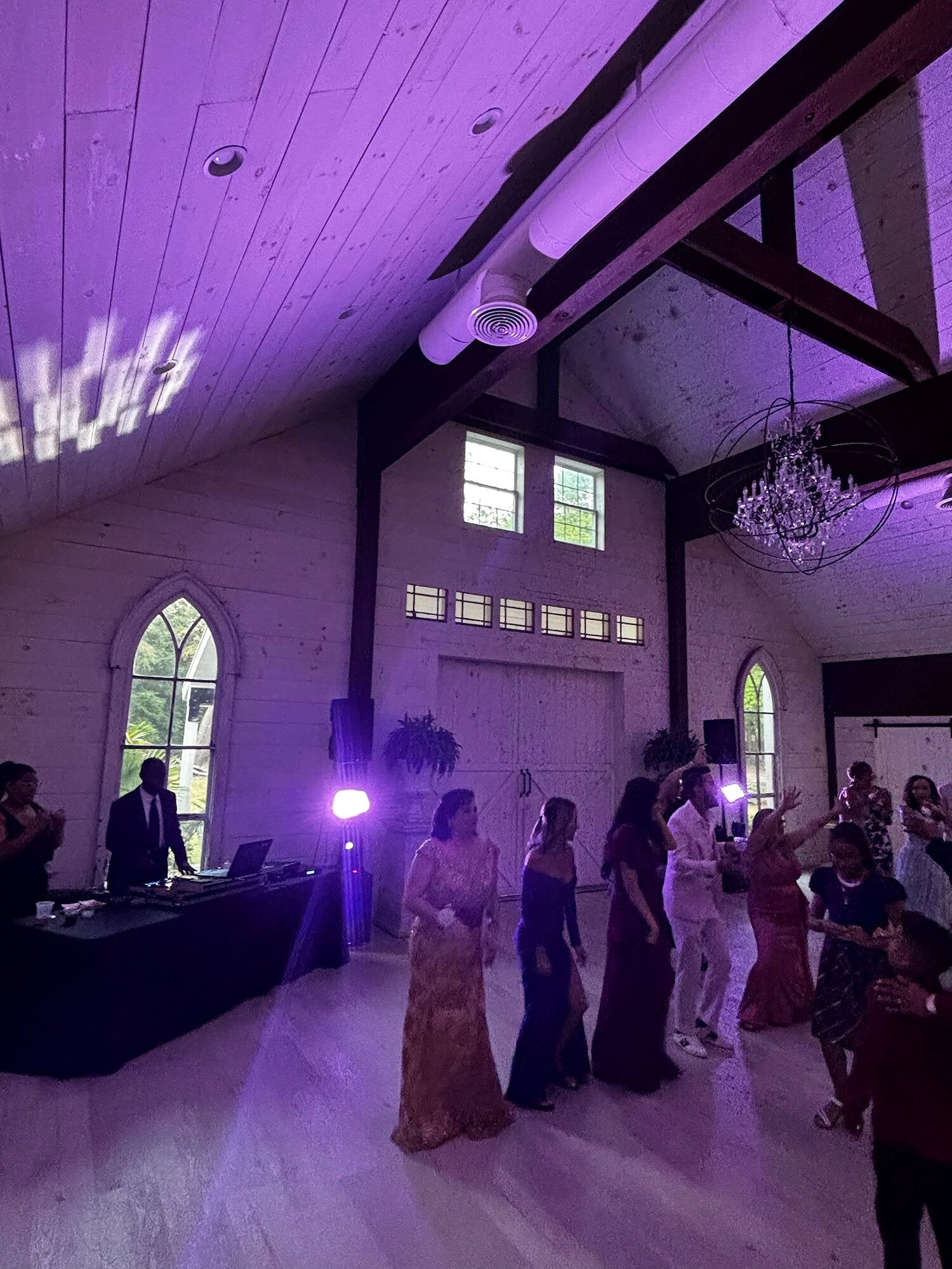 Guests dancing in a beamed chapel washed in purple uplighting by Sonar Audio Visual